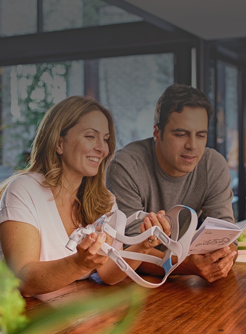 A man and women examining a ResMed CPAP mask and reading the user guide while leaning on a kitchen counter