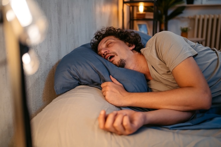 Young man sleeping in bed, snoring and having breathing problems