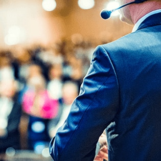 Someone giving a talk at a webinar, shown from behind with the audience blurred in the background